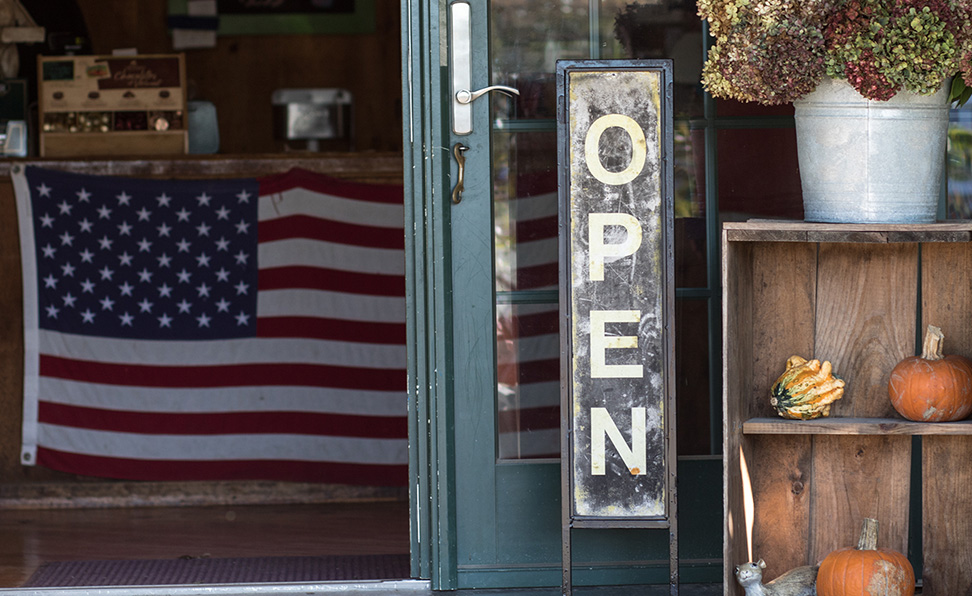 An “open” sign in front of an American business. The American flag is displayed inside the store.