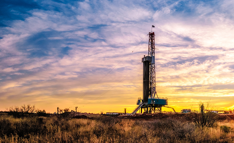 The sun sets behind a drilling rig